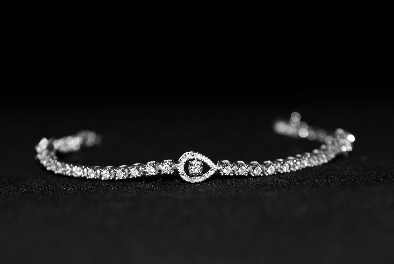 Diamond tennis bracelet with a circular centre design on a black background.